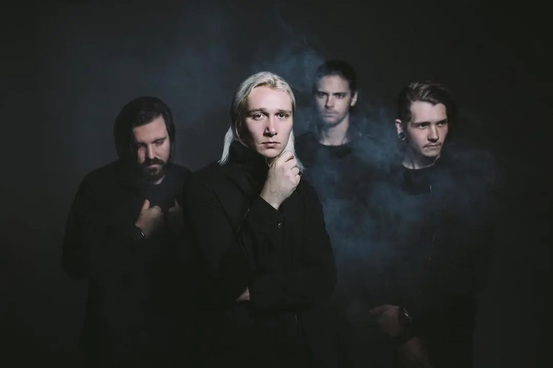 Four people pose in a dark studio; one sits on a stool while the others stand. Dramatic red and blue lighting casts shadows and highlights, creating a moody, artistic atmosphere.