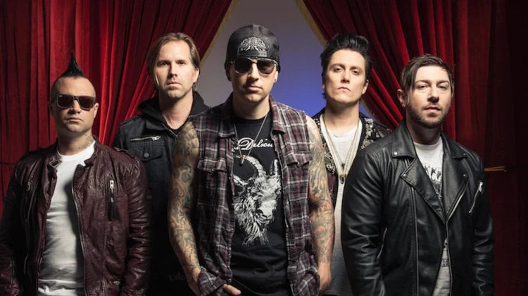Four men with tattoos and wearing hats, sunglasses, and casual clothing stand together in a group against a plain background, looking at the camera with serious expressions.