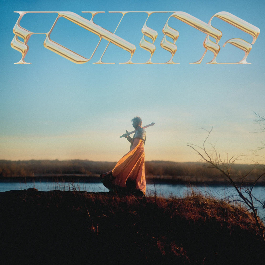A person in a flowing orange dress stands on a hill at sunset, playing a flute by a body of water. Abstract, shiny text appears at the top of the image against a clear sky.