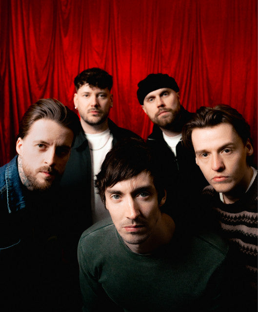 Five men look directly at the camera in a warmly lit room, with one reaching toward the lens. Below them is a bold black and white logo reading TRASH BOAT inside an oval.