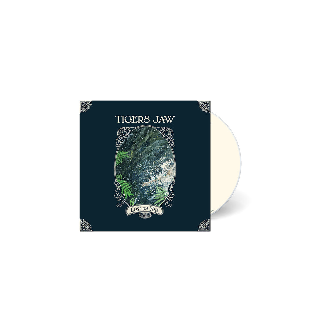 The Tigers Jaw album Lost on You features a dark cover with ornate silver corners, an oval frame highlighting a green and blue nature scene, and a small banner at the bottom displaying the title.