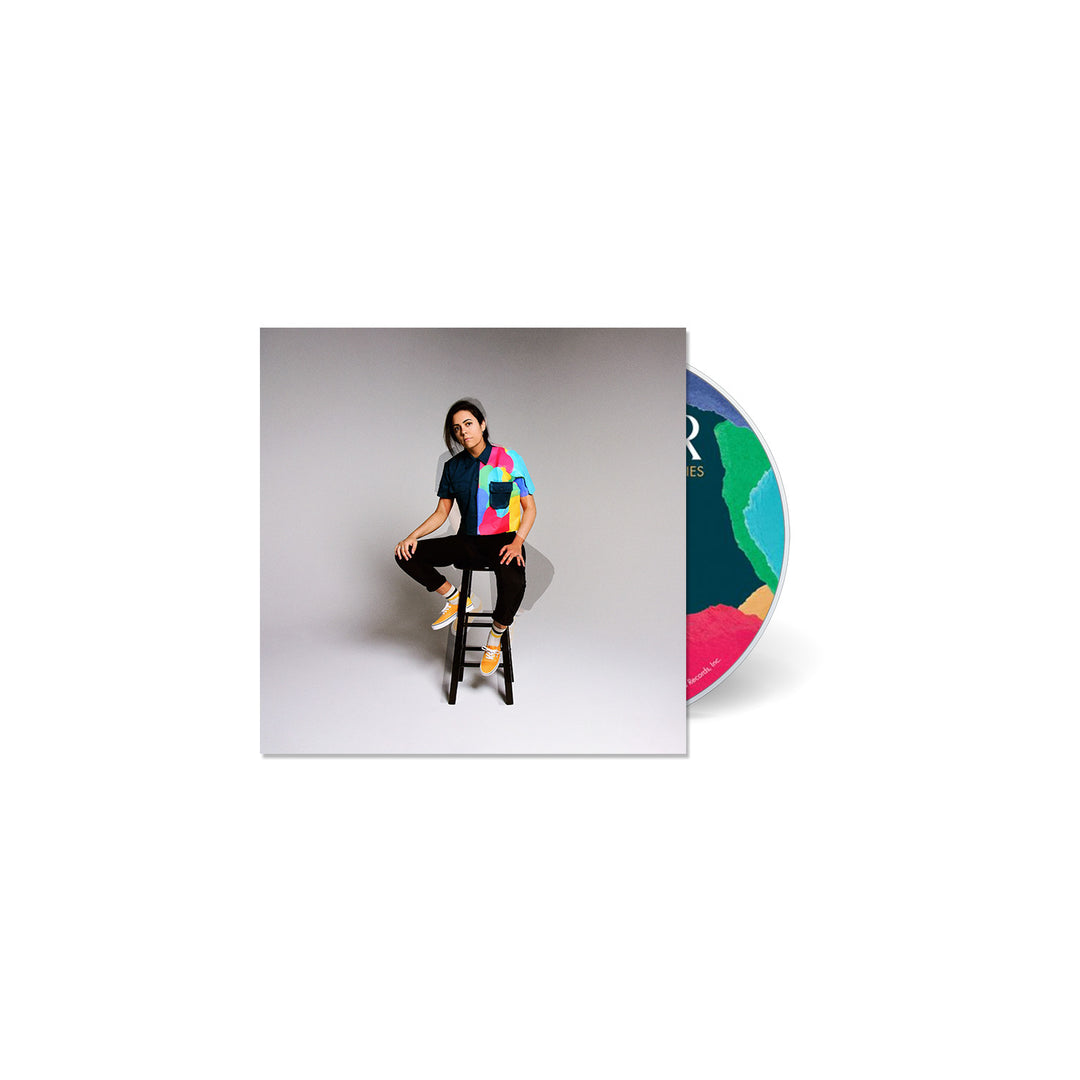 Illuminati Hotties’ Cant Be Still CD case shows a person on a stool against a plain background; the partially visible CD displays colorful, abstract designs. Releases August 23rd, 2024.