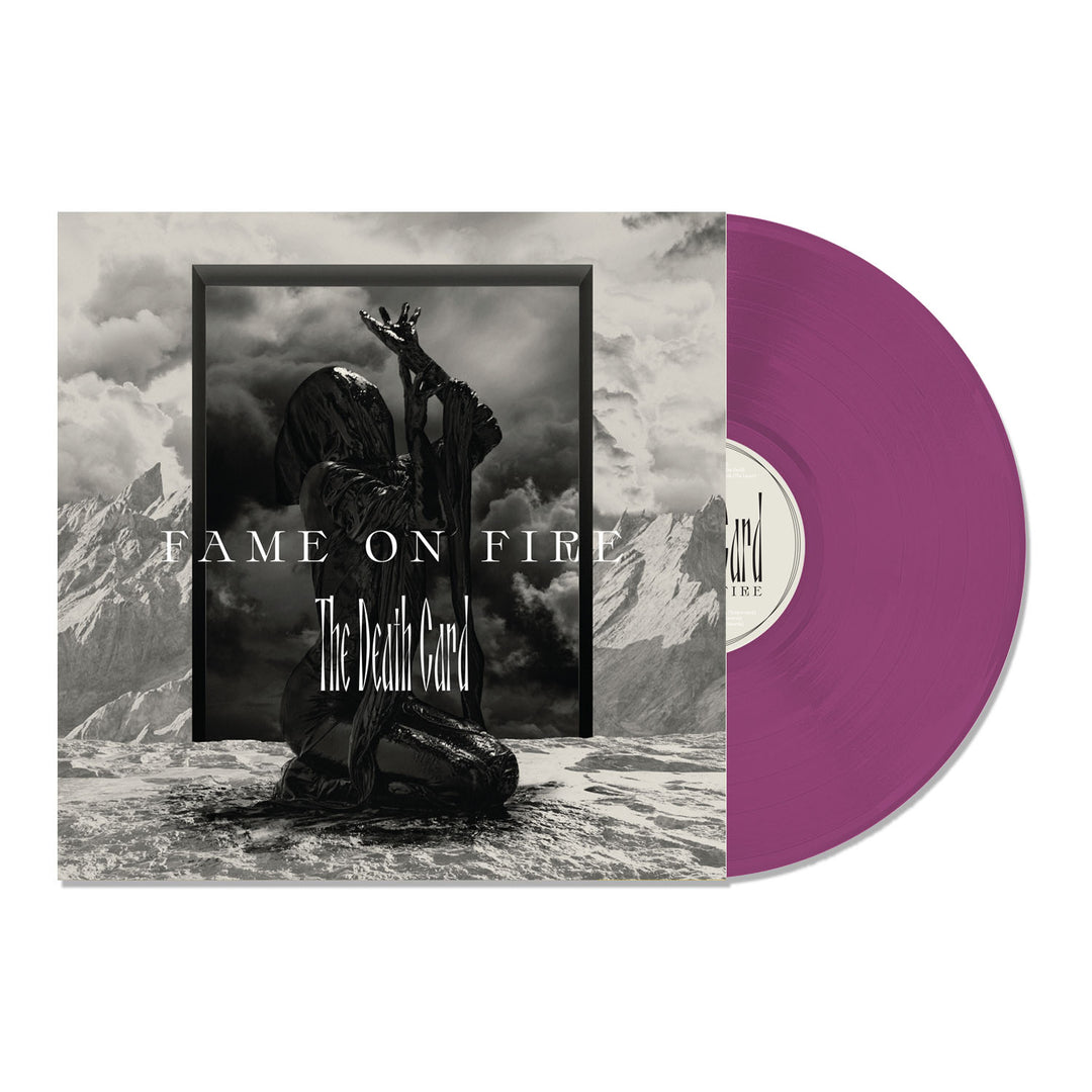 A purple vinyl record partially slides out of its album cover, which features a dark, cloaked figure with raised arms in a mountainous landscape. This limited edition release displays Fame On Fire and The Death Card in bold lettering.