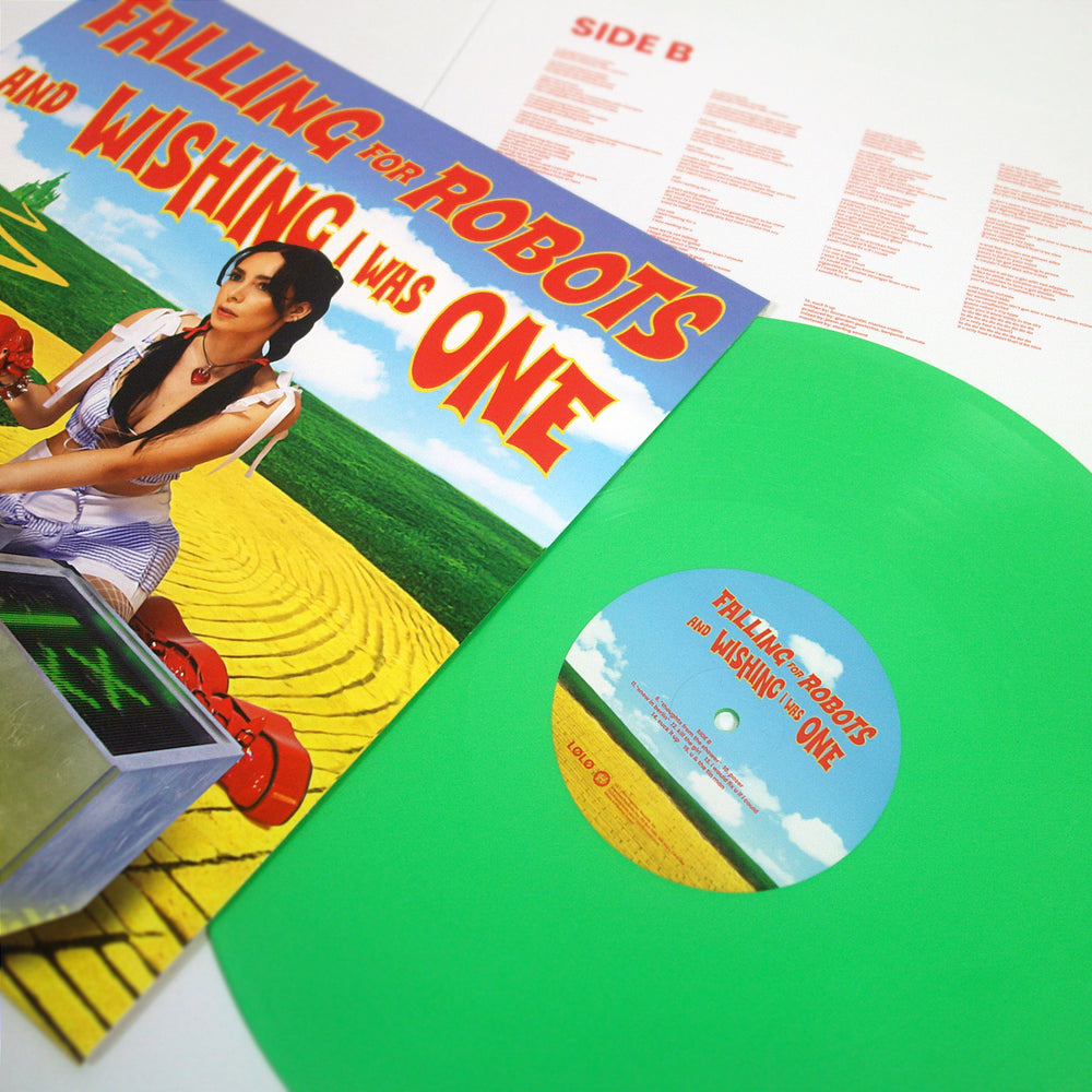 A vibrant green vinyl record from L0L0 sits next to its colorful album cover, showing a woman in a yellow field under a blue sky with bold text: FALLING FOR ROBOTS AND WISHING I WAS ONE.