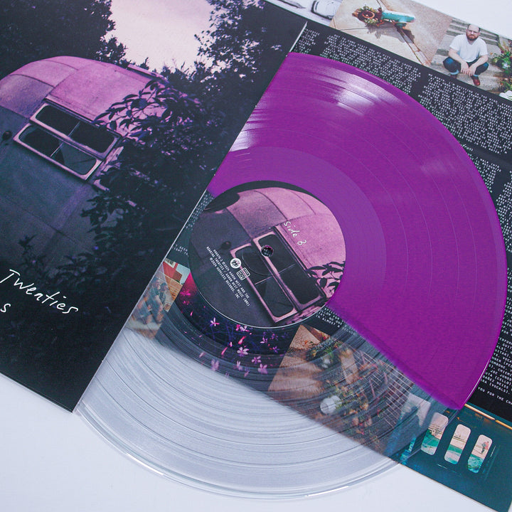 A half clear, half purple Aaron West and the Roaring Twenties vinyl rests on its sleeve with an old camper van in Monongahela Park. An insert about Roman Candles with images and text peeks out from beneath the record.