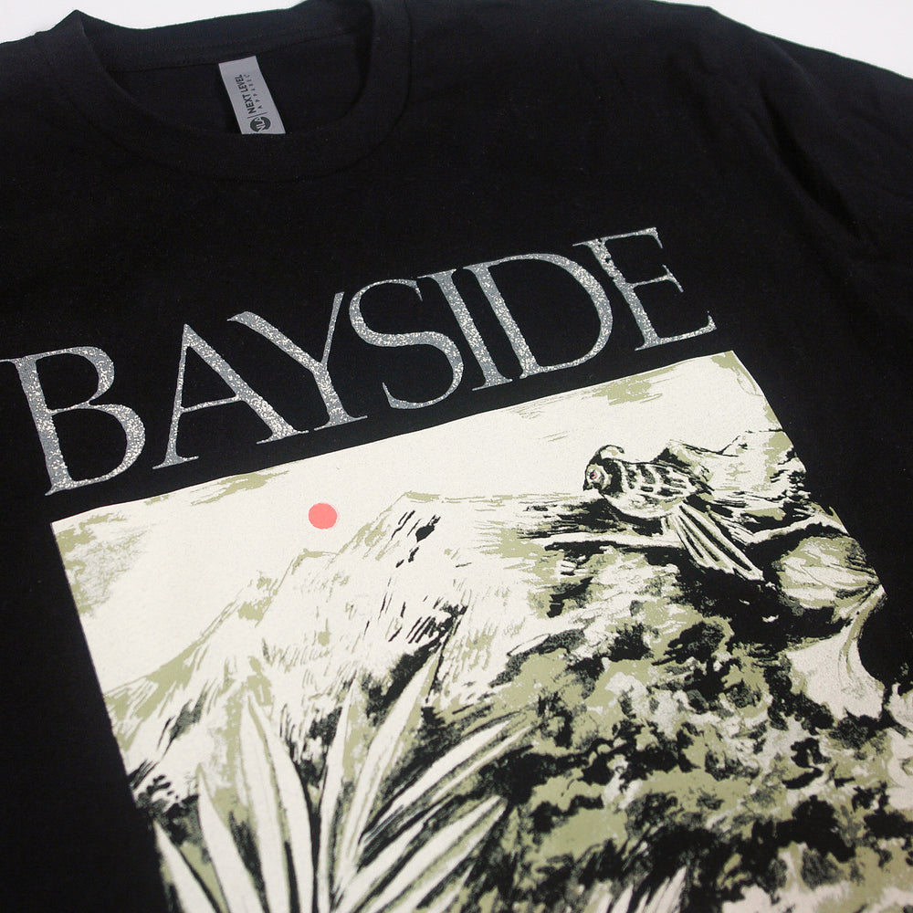 A black Bayside t-shirt displays BAYSIDE in bold white letters with a bird on rocks, mountains, plants, and a red sun—a unique design available only here.