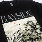 A black Bayside t-shirt displays BAYSIDE in bold white letters with a bird on rocks, mountains, plants, and a red sun—a unique design available only here.