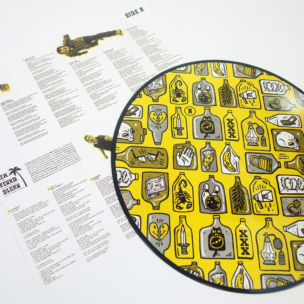 A printed sheet with song lyrics and illustrations lies next to a circular yellow New Found Glory item decorated with cartoon bottles, plants, and objects—referencing tracks like The Cheapest Thrill—on a white background.