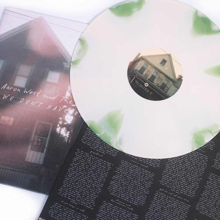 A pale white and green vinyl by Aaron West and the Roaring Twenties features a center label with part of a house, sits on a sleeve with house photo and handwriting, and includes lyrics plus a bonus track printed on the inner sleeve.