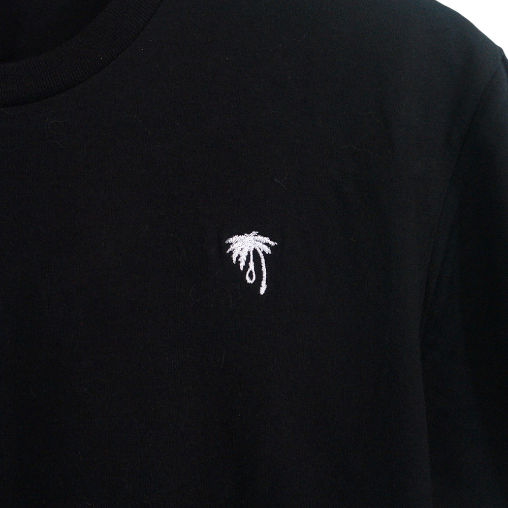 A close-up of a black Trophy Eyes shirt with a small white embroidered black palm tree on the chest—perfect for fans of subtle palm tree designs.