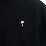 A close-up of a black Trophy Eyes shirt with a small white embroidered black palm tree on the chest—perfect for fans of subtle palm tree designs.
