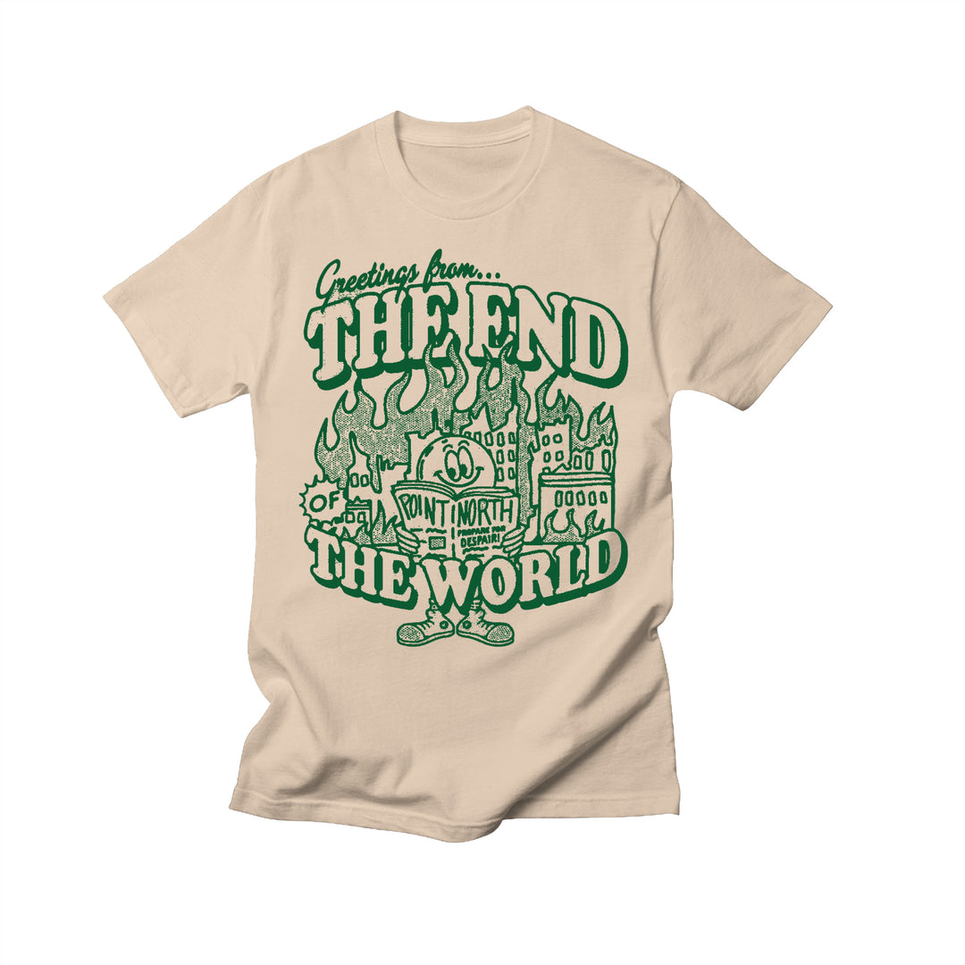 Point North cream Next Level T-shirt with a green illustration of a burning city and cartoon character, featuring bold “Greetings from… THE END OF THE WORLD” and “POINT NORTH” print in the center.