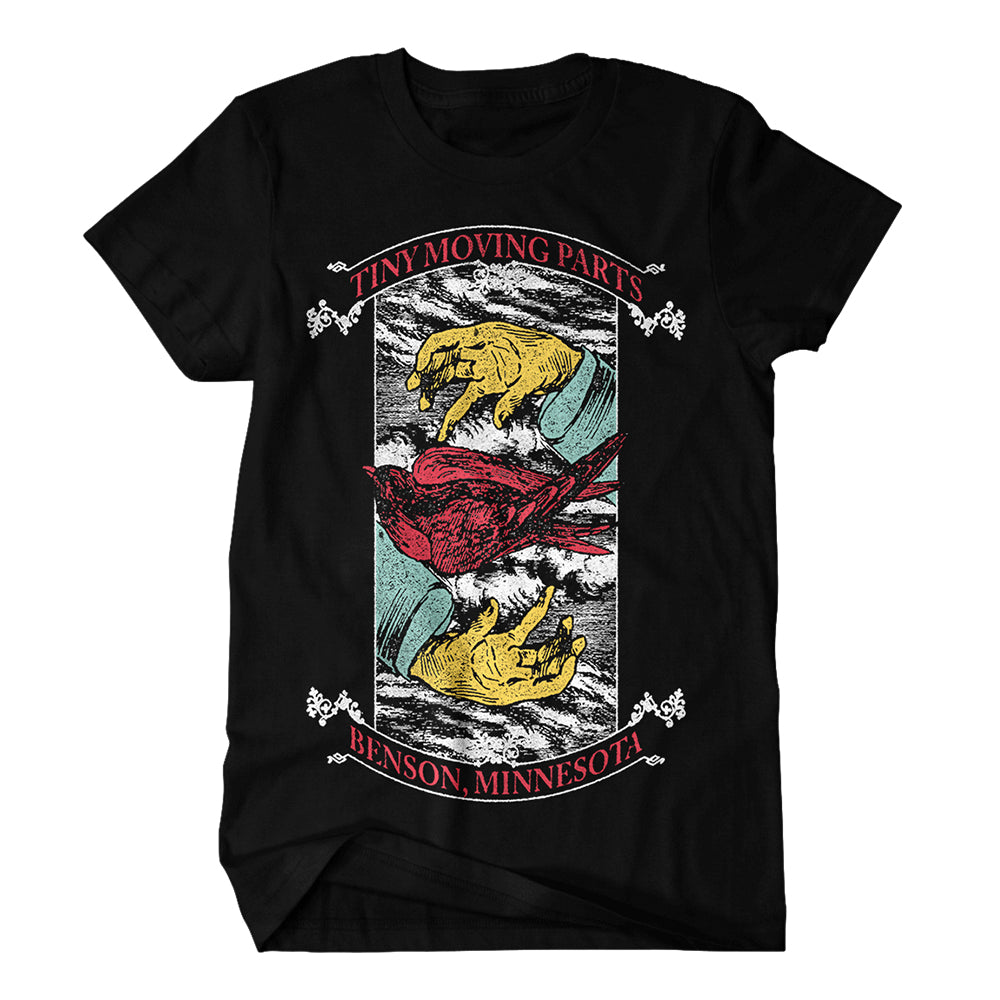 Black T-shirt by Tiny Moving Parts shows yellow-gloved hands holding a Floating Bird, with “Tiny Moving Parts” above and “Benson, Minnesota” below, all inside a detailed rectangular frame.