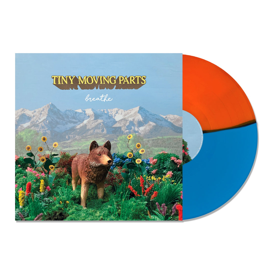 An orange and blue vinyl record lies next to its cover, which shows a toy wolf in a bright flower field with mountains and sky. The album title Breathe and band name Tiny Moving Parts appear above.