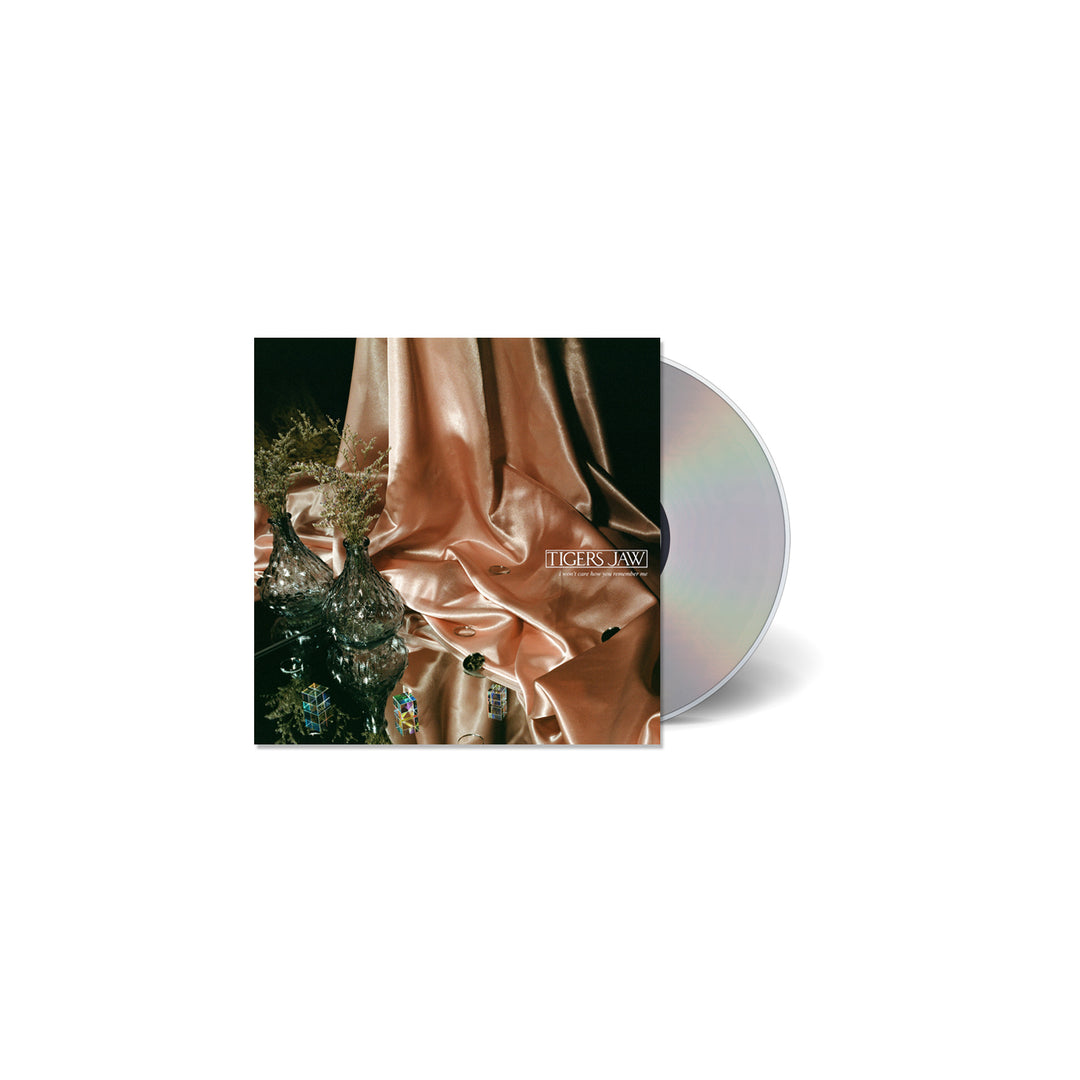 A CD by Tigers Jaw comes in a clear case with an album cover showing pink satin fabric, glass vases, and flowers. TIGERS JAW is featured in white text on the fabric. The dark background highlights its March 5th, 2021 release date.