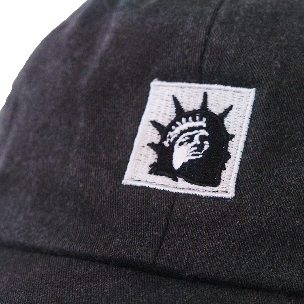 Close-up of a black Trophy Eyes Dad Hat with an embroidered patch showing a stylized black and white Statue of Liberty face.