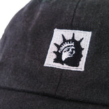 Close-up of a black Trophy Eyes Dad Hat with an embroidered patch showing a stylized black and white Statue of Liberty face.