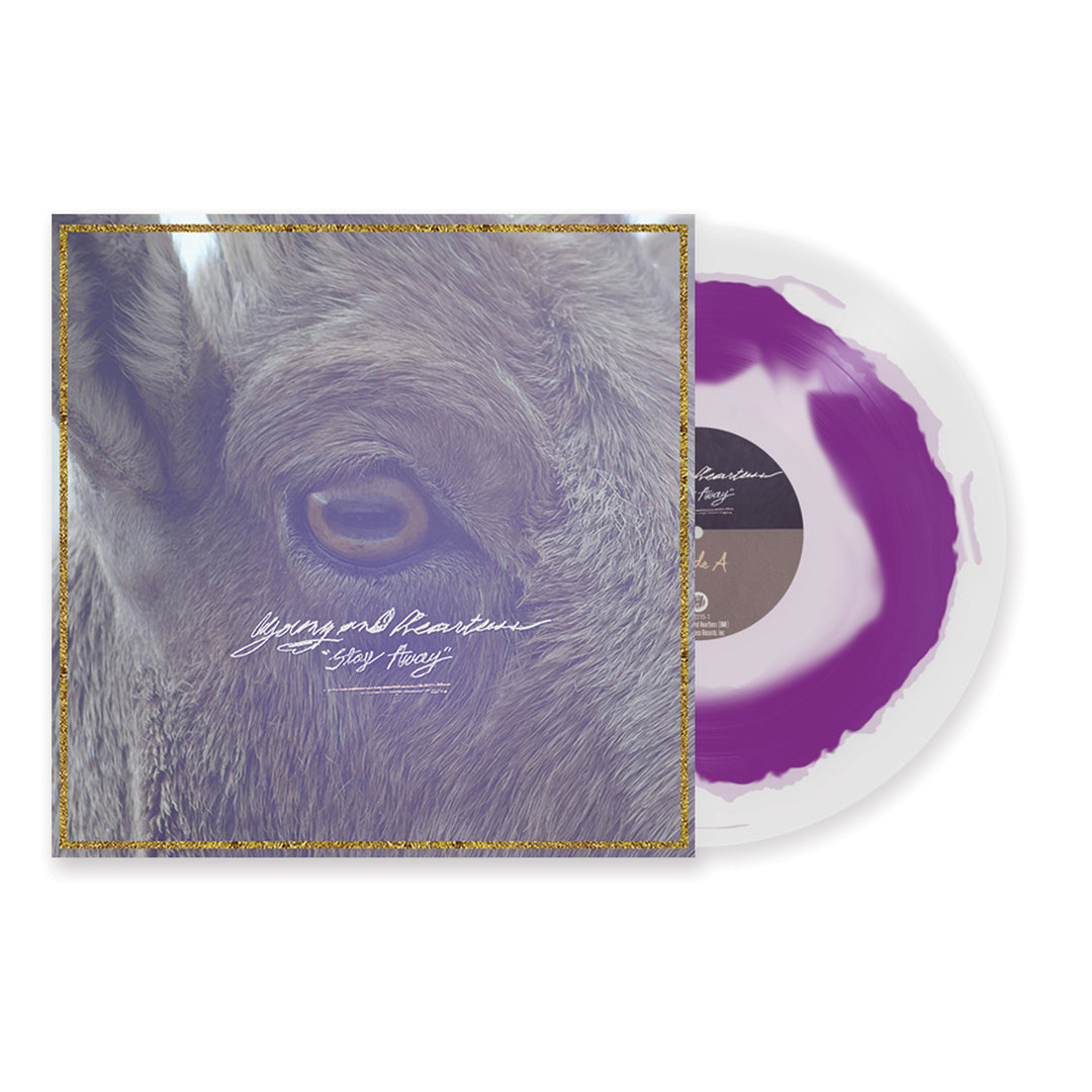 A purple and white splatter vinyl record partially slides out of an album cover featuring a close-up of an animal’s eye and fur, with cursive text reading Young And Heartless Stay Away and the track list on the back.