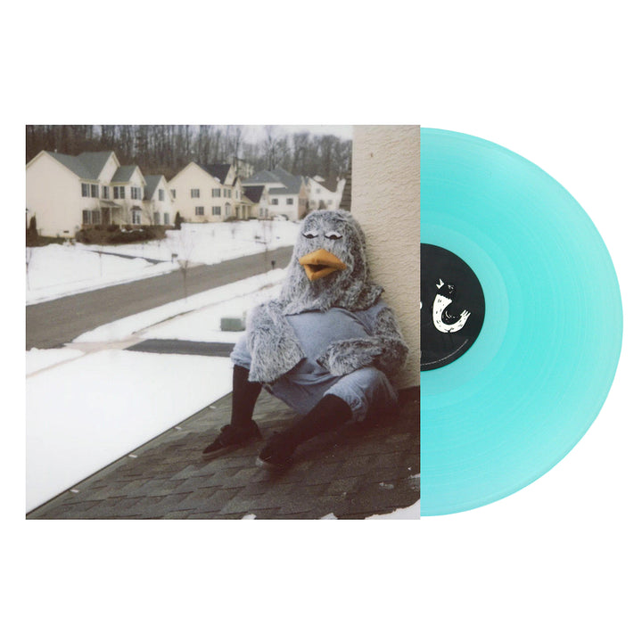 A turquoise vinyl record by The Wonder Years partially covers an album cover depicting a person in a gray bird costume sitting on a snowy rooftop, with suburban houses visible in the background.