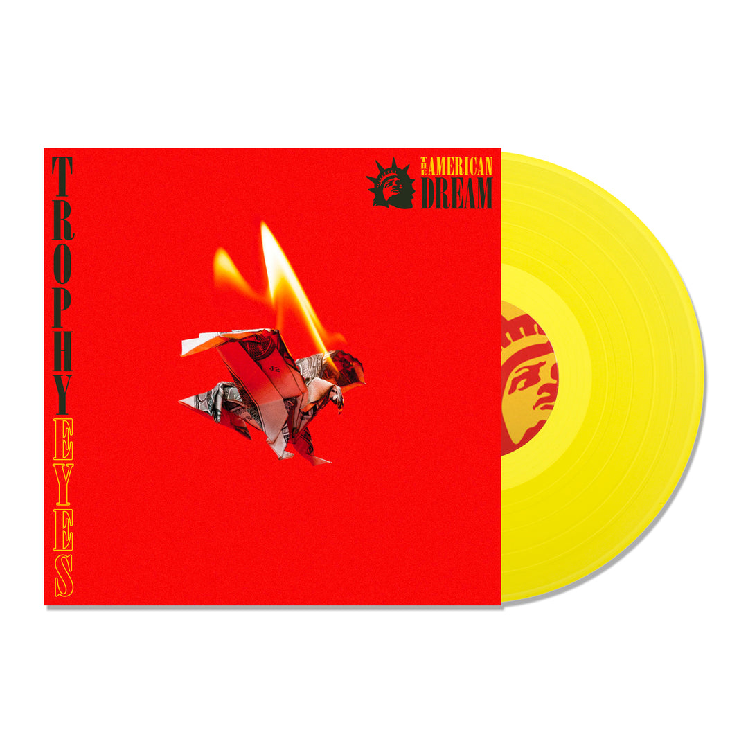 A bright transparent yellow vinyl record partially slides out of the red Trophy Eyes LP cover featuring Trophy Eyes and American Dream text, a burning photo, and a stylized face in one corner.