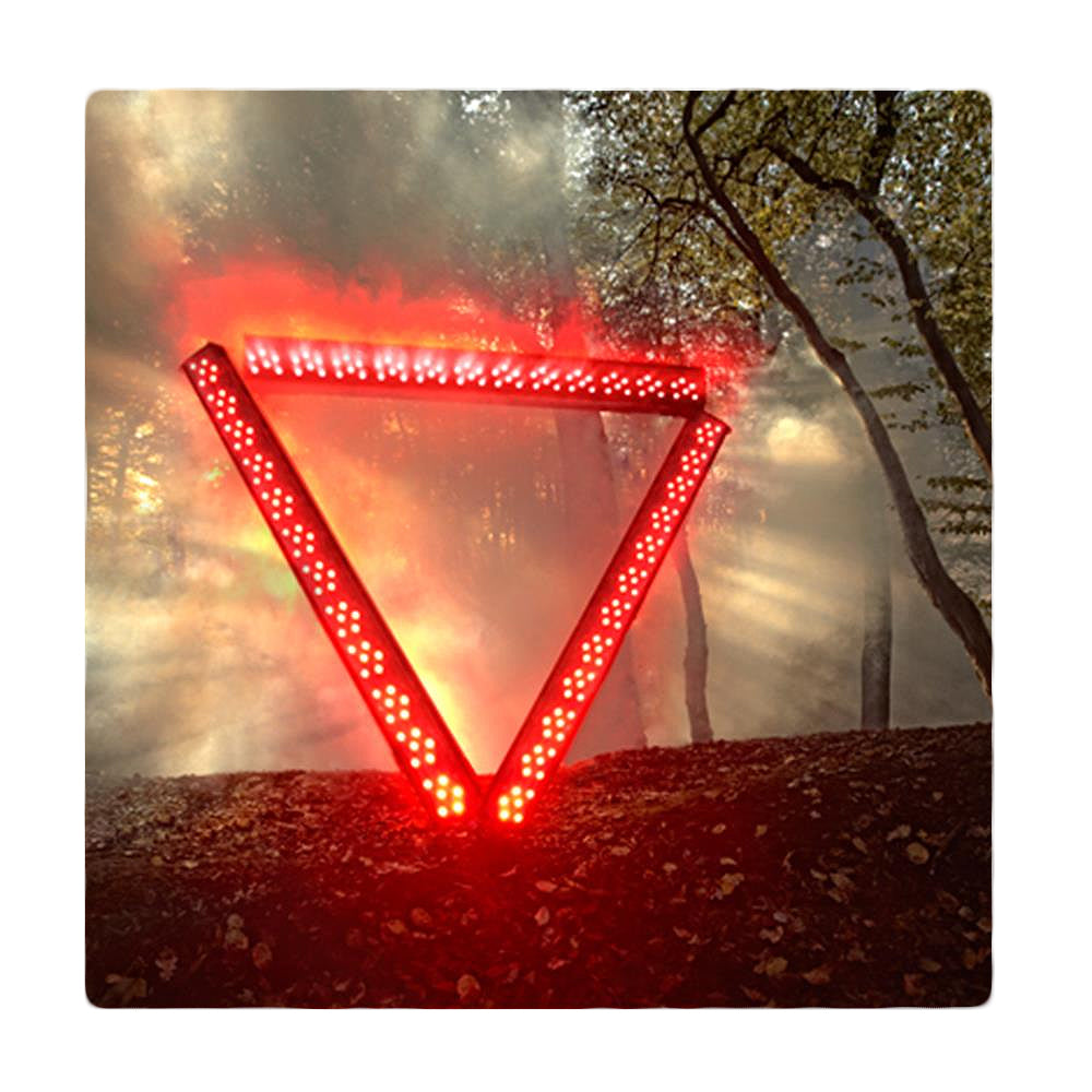 A glowing red, illuminated triangle stands upright in a misty forest—like a warning from the Enter Shikari system—as beams of sunlight stream through the trees in the background.