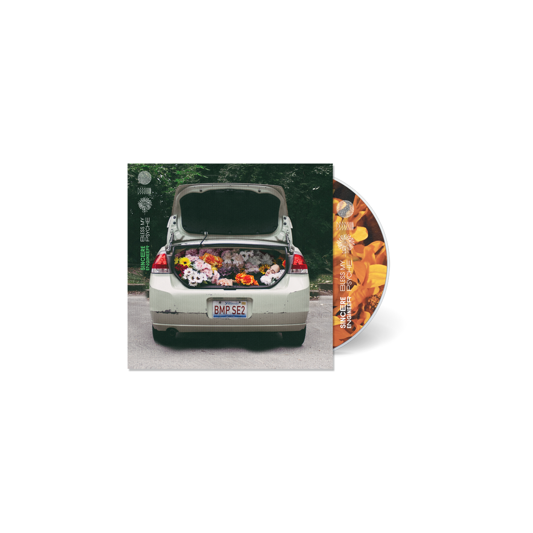A car with an open trunk filled with colorful flowers is parked on a street. To the right, a Sincere Engineer CD for the Bless My Psyche album, featuring an orange floral design, is partially visible next to the album cover.