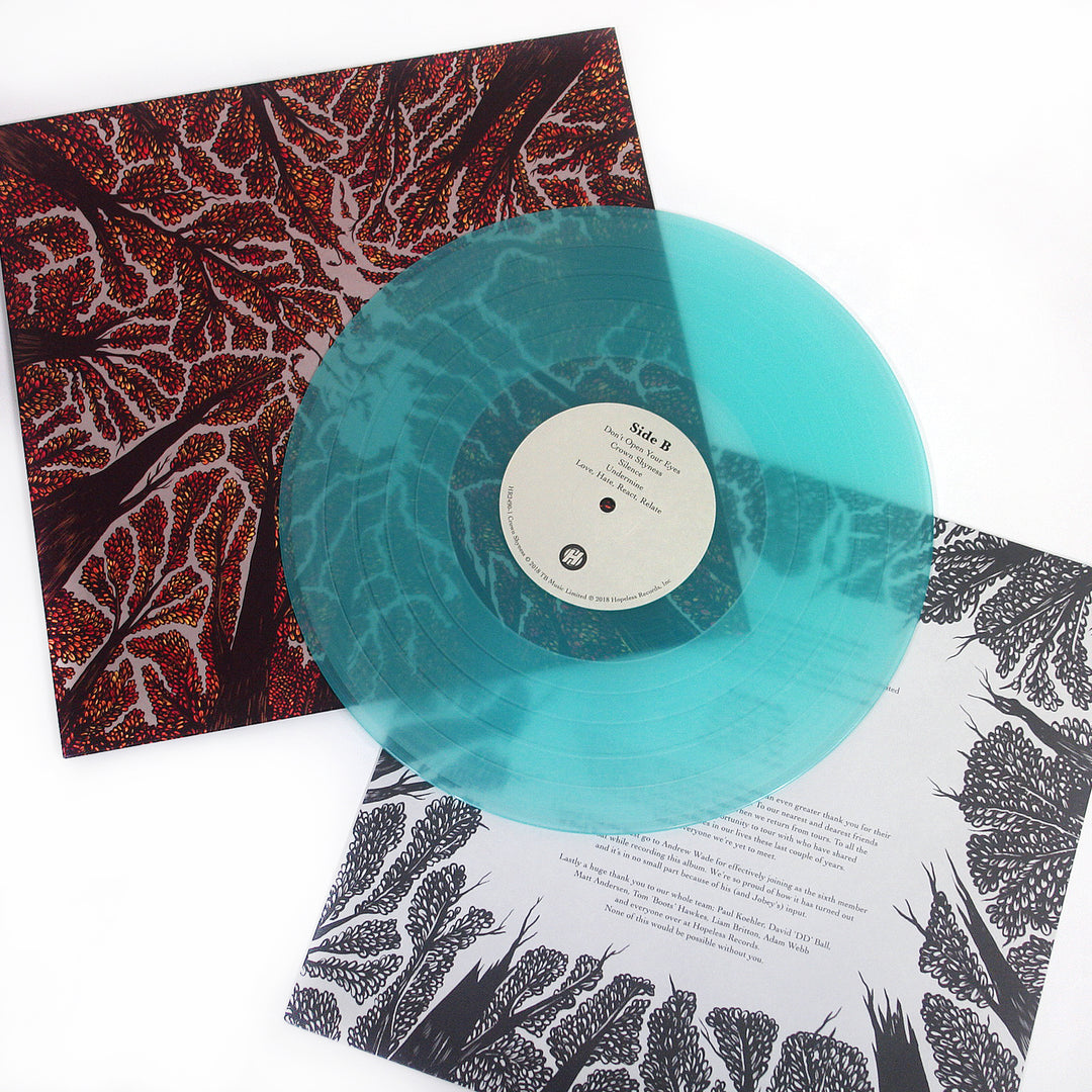 A translucent turquoise Trash Boat vinyl titled Controlled Burn rests on a black-and-red album cover with abstract tree branches and a white insert featuring black botanical illustrations and printed text.