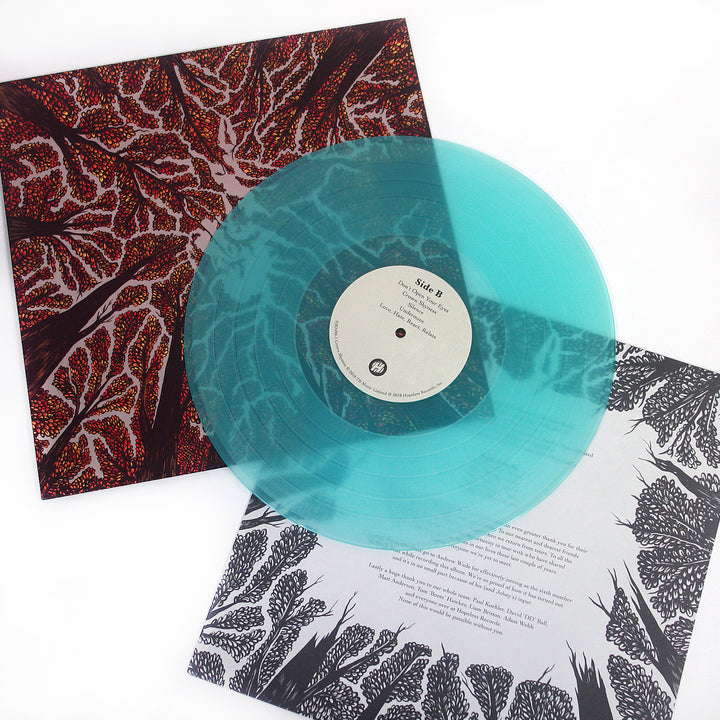 A translucent turquoise Trash Boat vinyl titled Controlled Burn rests on a black-and-red album cover with abstract tree branches and a white insert featuring black botanical illustrations and printed text.