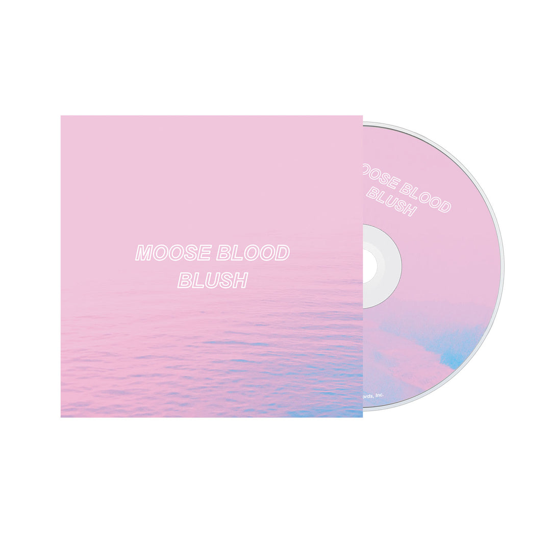 A CD partially outside its case, both with a pink gradient design. The cover shows Moose Blood Blush in white capitals over calm water, referencing the Blush CD tracklist inside from the brand Moose Blood.