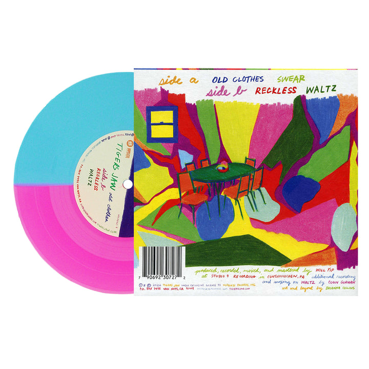 A colorful vinyl record, half blue and neon magenta, by Tigers Jaw rests next to its vivid abstract sleeve—featuring a bright table and chairs illustration with the tracklisting and production details displayed.