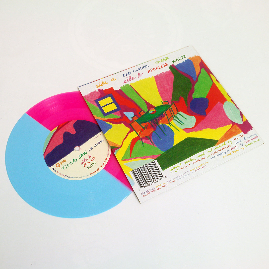 A vibrant 7-inch vinyl from Tigers Jaw, in half blue and neon magenta, sits next to its abstract cover with a green chair and table; Side A reads old clothes, with track details on the back.