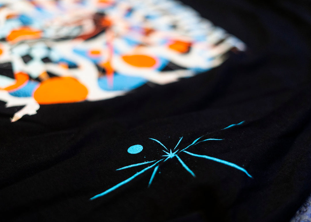 Close-up of a black Trash Boat long sleeve featuring a colorful abstract design with orange, blue, and white shapes, plus a small blue starburst and dot pattern—ideal band merch for any fan.