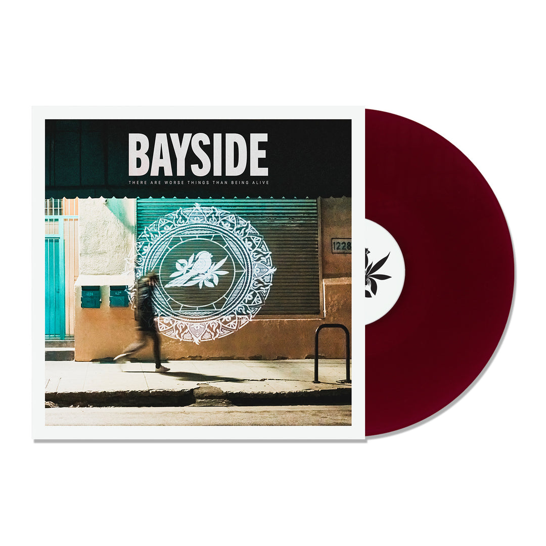 A maroon vinyl record slides out of a Bayside album cover, showing a blurred figure walking by a building adorned with a large white bird and wreath design.