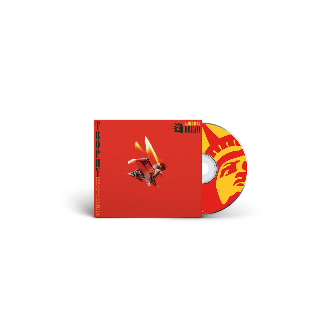 A red CD case and disc by Trophy Eyes, featuring a flaming-winged figure. The Trophy disc shows a stylized yellow Statue of Liberty face and an American Dream-inspired tracklist.