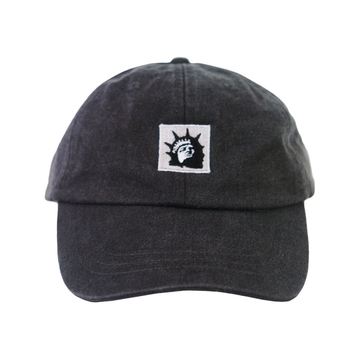 A black dad hat by Trophy Eyes with a white square patch featuring a black Statue of Liberty head graphic—ideal for anyone seeking a unique, classic statue hat.