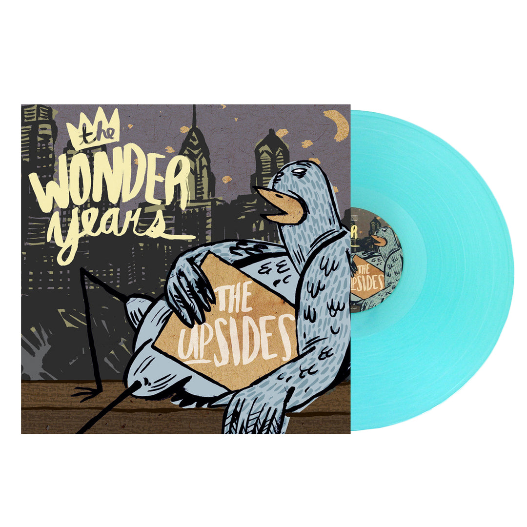 A light blue vinyl record by The Wonder Years slides from its cover, which shows illustrated city buildings at night, a pigeon with a box labeled The Upsides, and bold lettering referencing Logan Circle.