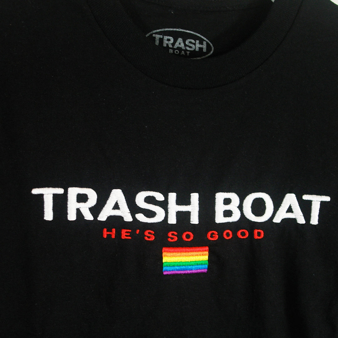 Trash Boat black shirt with white TRASH BOAT text, red HE’S SO GOOD, and a small rainbow pride flag patch. Available in sizes up to X-Large.
