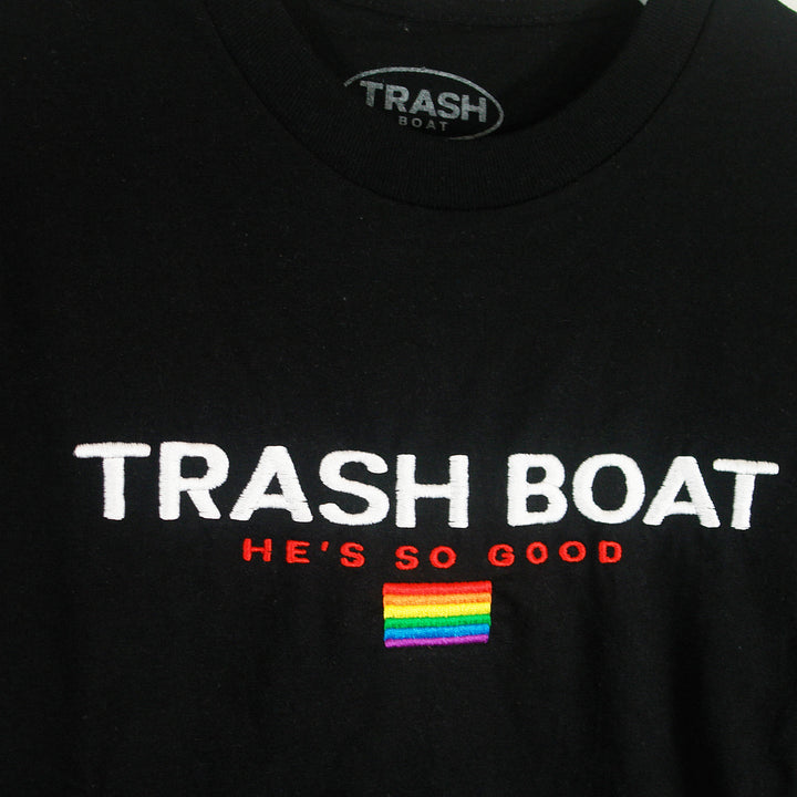 Trash Boat black shirt with white TRASH BOAT text, red HE’S SO GOOD, and a small rainbow pride flag patch. Available in sizes up to X-Large.