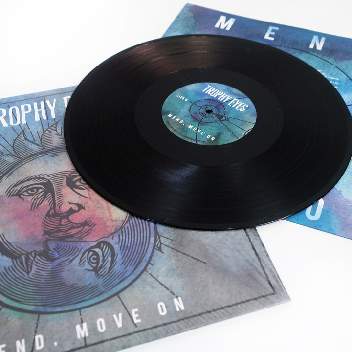 A black vinyl record by Trophy Eyes rests on its illustrated album cover, displaying a stylized face in purple and blue. The center label features the Trophy Eyes brand name, with the Mend Move On tracklist visible.