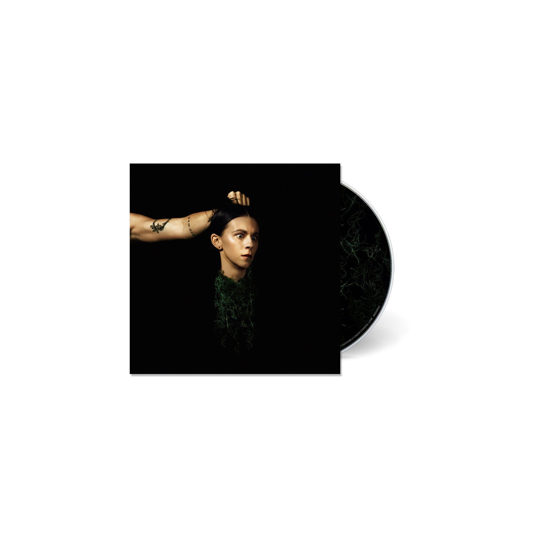 A PVRIS CD case features cover art of an arm lifting a short dark-haired head with a serious look against a black background. The tracklisting isnt visible, and the CD is partially shown.