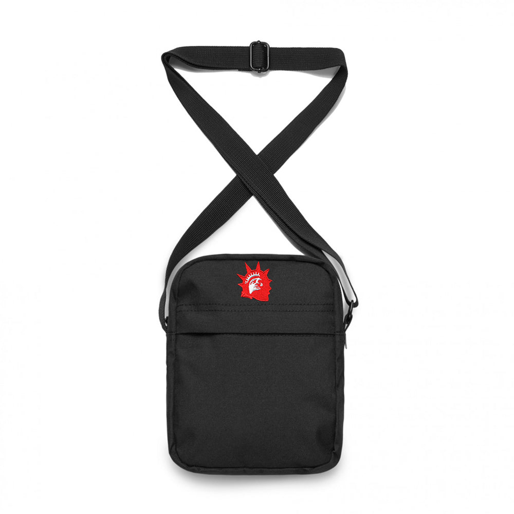 Trophy Eyes black shoulder bag with an adjustable strap, featuring a small red Statue of Liberty head graphic on the upper front. The bag has a simple, minimalist design.